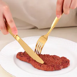 Gros plan d'un couteau et d'une fourchette dorés coupant un steak avec manche rayé