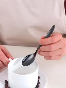 Close-up of a hand holding a polished black stainless steel spoon with coffee set
