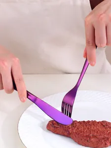 Detailed view of purple titanium coated stainless steel knife and fork slicing a steak