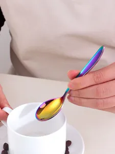 Close-up of a rainbow titanium coated stainless steel spoon held next to a coffee cup