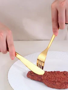 Detail of model using gold stainless steel knife and fork to cut steak on a white plate