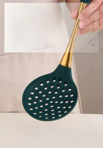 Detail of dark green silicone slotted spoon with gold stainless steel handle and round holes