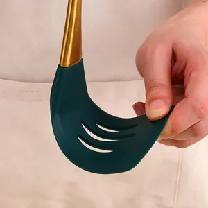 Flexible dark green silicone slotted turner with gold handle showing heat resistance