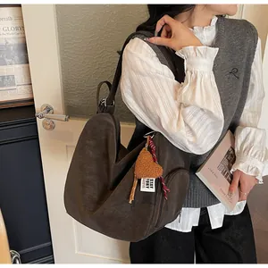 Braune Hobo-Tasche aus Wildlederimitat mit Herzanhänger am Model in Freizeitkleidung