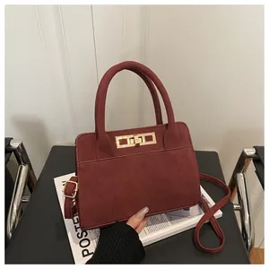 Dettaglio borsa quadrata in camoscio bordeaux con chiusura girevole oro e doppi manici