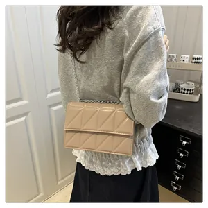 Detail of beige flap bag with triangle quilted patterns and silver chain shoulder strap