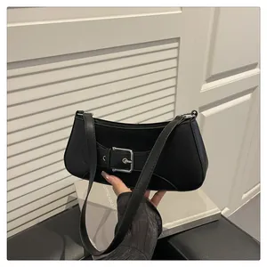 Detalle de bolso baguette negro con hebilla plateada y correa de hombro curva con estilo