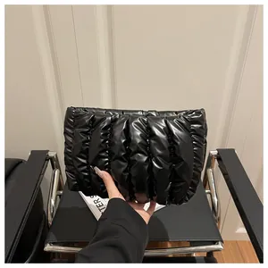 Chic black pleated puffer clutch bag held in hand, featuring a shiny quilted texture