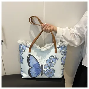 Close-up of a floral tote bag with blue butterfly print and fringe details