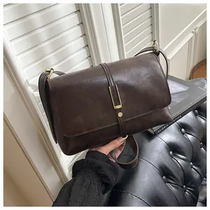 Detail of vintage brown leather bag showing gold buckle and matte texture on a sofa