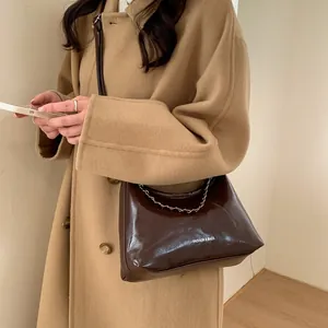 Détail du sac bandoulière en cuir verni marron foncé avec chaîne argentée et logo