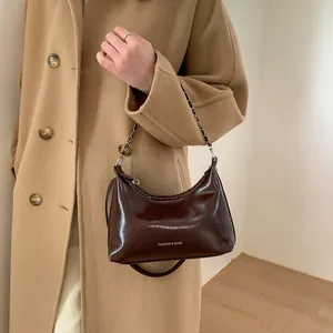 Détail du sac bandoulière en cuir verni marron foncé avec sangle en chaîne métal