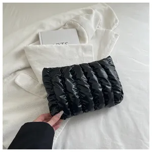 Detail der schwarzen glänzenden Clutch mit Faltenstruktur auf weißem Cordstoff