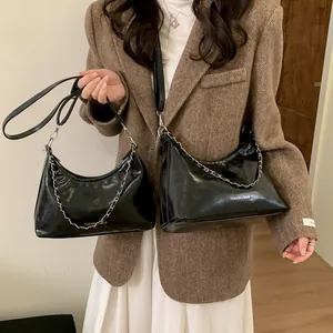 Sac à bandoulière noir brillant en forme de croissant avec chaîne argentée sur un blazer
