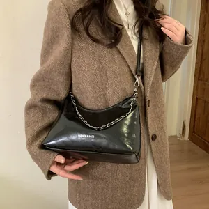 Détail du sac bandoulière en cuir verni noir avec chaîne sur un blazer à chevrons marron