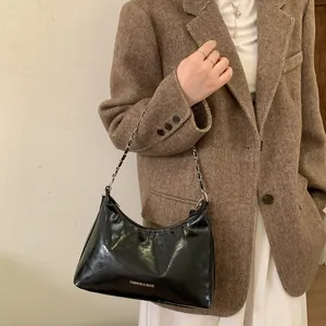 Sac à bandoulière noir brillant avec chaîne argentée porté sur un blazer en laine