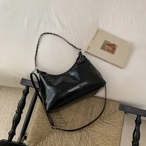 Détail du sac en cuir PU noir avec chaîne argentée et logo textuel posé sur une chaise
