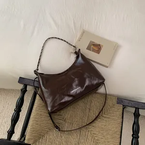 Détail d'un sac à main marron foncé en cuir verni avec chaîne argentée sur une chaise