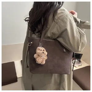 Detail of dark brown tote bag with suede texture and a cute plush bear charm on a trench coat