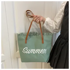 Détail du cabas en toile verte avec bords effilochés, broderie Summer et anses en cuir
