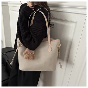 Detail der beigen Shopper-Tasche mit braunem Plüschbär-Anhänger auf schwarzem Pullover