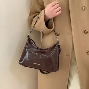 Petit sac carré marron brillant avec bandoulière chaîne porté sur un manteau en laine