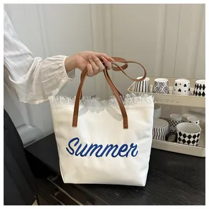 Gros plan du sac cabas en toile blanche avec broderie Summer bleue et franges blanches