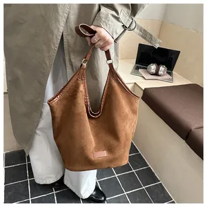 Sac fourre-tout en daim marron présenté avec un trench-coat kaki et un ordinateur portable