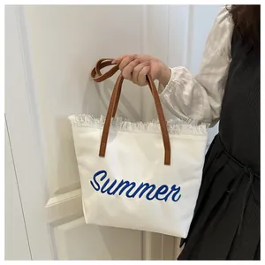Détail du sac fourre-tout en toile blanche avec broderie Summer et anse en cuir brun