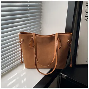 Detail of a brown suede tote bag with leather trim and gold hardware by a window