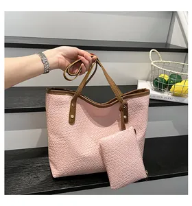 Pink woven tote bag with matching zippered pouch and dark brown handles held by hand
