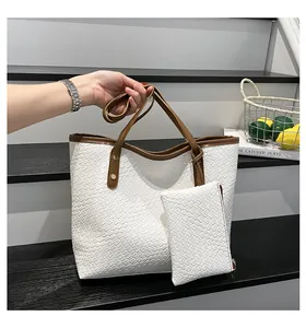 Detail of white woven tote bag featuring brown leather straps and gold metal rivets