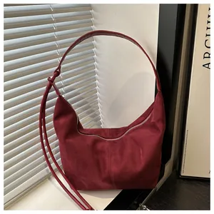 Close-up of burgundy suede crescent bag with silver zipper and knotted strap detail