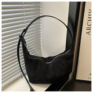 Detail of black suede hobo bag with zipper and slender leather strap on minimalist background