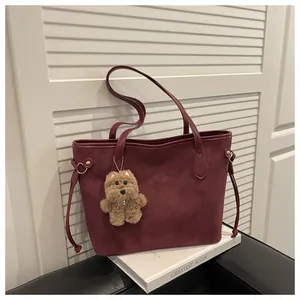 Details einer burgunderroten Wildleder-Tote-Bag mit braunem Bärenanhänger und Griffen