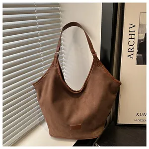 Gros plan d'un sac d'épaule en daim marron avec passepoil en cuir et patch minimaliste