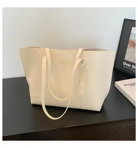 Detail of cream tote bag featuring golden logo and side tag on dark wooden surface