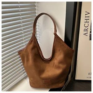 Détail du sac cabas en daim marron montrant la texture fine et l'écusson rectangulaire