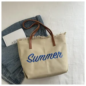 Détail du sac en toile beige avec broderie Summer bleue et bordures à franges