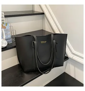 Black matte leather tote bag with gold lettering shown in a stylish indoor setting