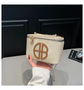 Gros plan d'un mini sac en cuir beige avec bandoulière dorée et détail de logo rond