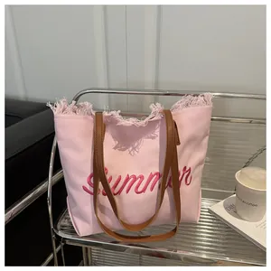 Détail du sac cabas en toile rose avec broderie Summer et bords effilochés sur étagère