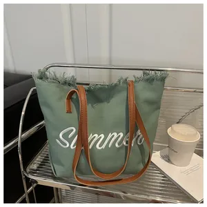 Détail du sac cabas en toile verte avec broderie Summer et bords effilochés sur étagère