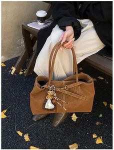 Detail of a brown suede tote bag featuring a heart mirror charm and white stitching