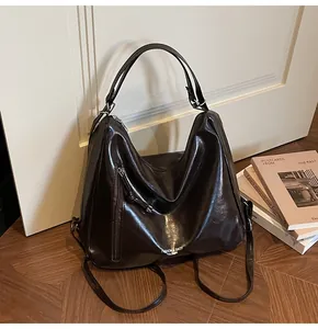 Close-up of a dark brown glossy leather tote bag showing a vertical zipper and wide strap
