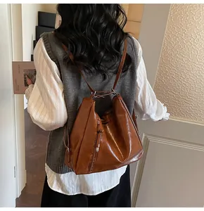 Detailed view of brown glossy leather backpack with soft texture and drawstring on model