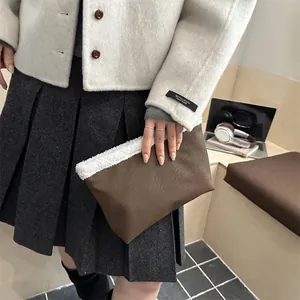 Pochette in pelle marrone con bordo in peluche bianco in un elegante contesto lifestyle