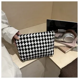Detail of checkered knit clutch bag held by model featuring soft black and white weave