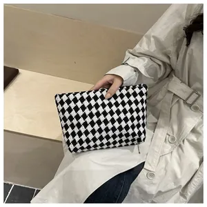 Detail of a chic black and white checkered clutch bag held with a beige trench coat