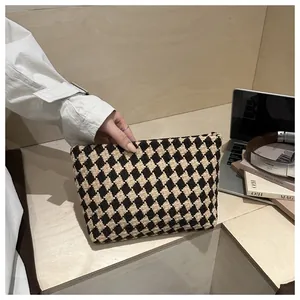 Detail of hand-held woven brown and beige checkerboard clutch bag in a modern setting